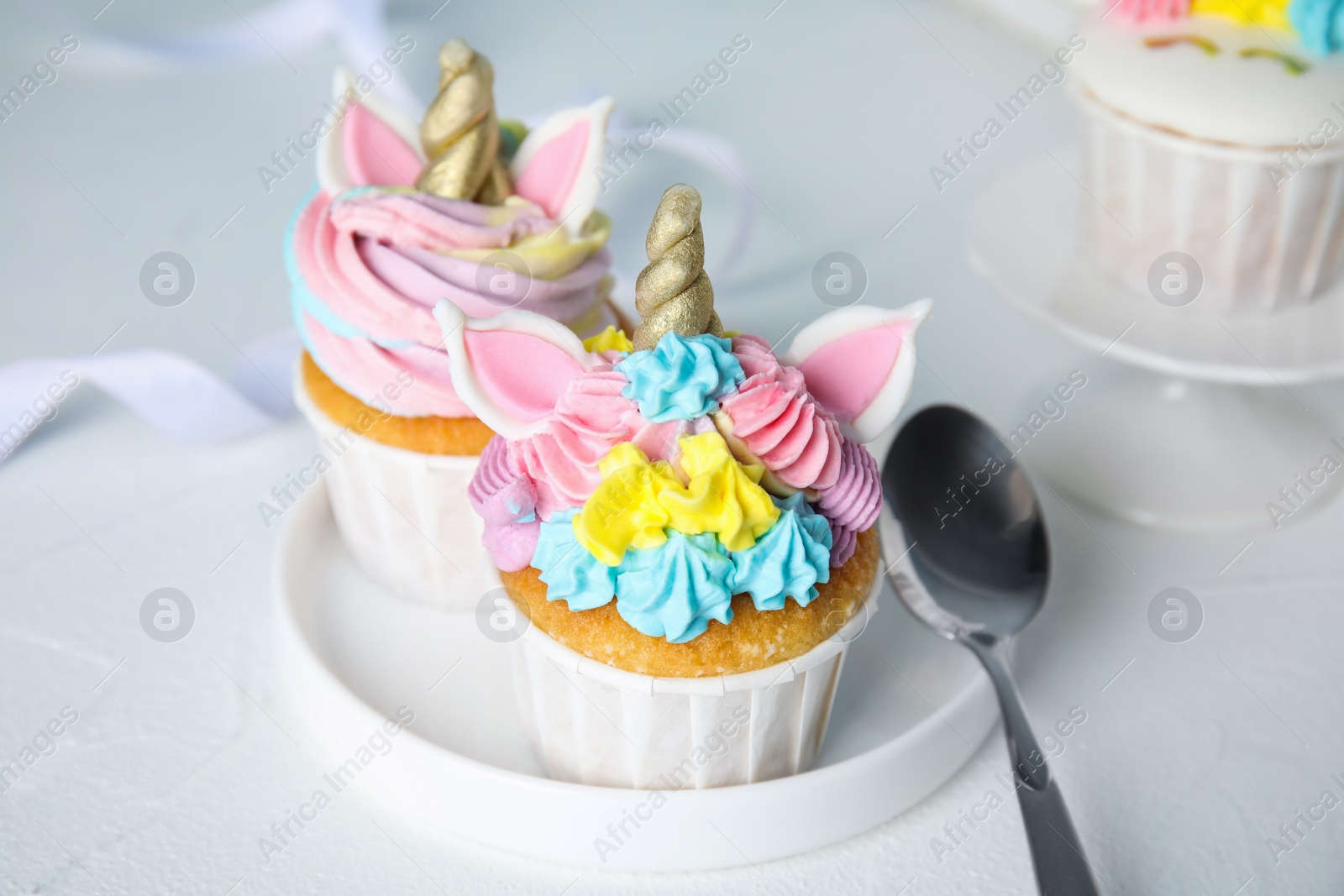Photo of Plate with two cute sweet unicorn cupcakes on white table, closeup
