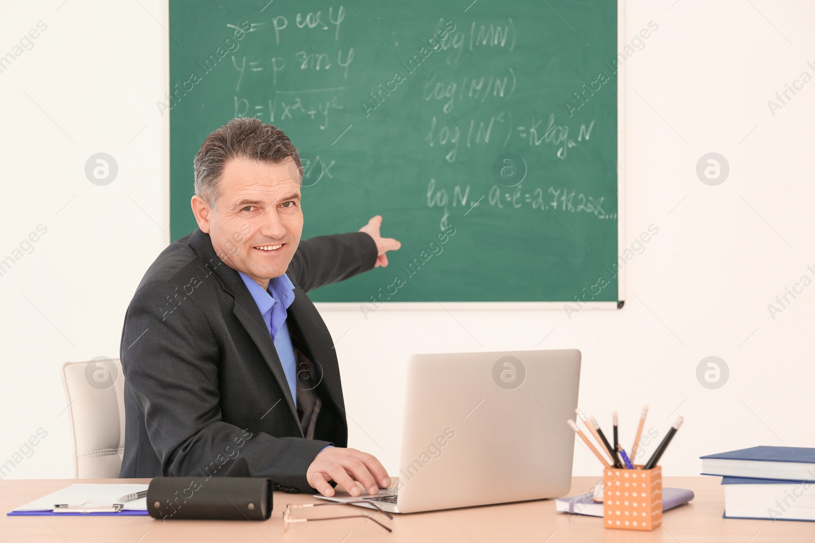 Photo of Male teacher working with laptop at table in classroom