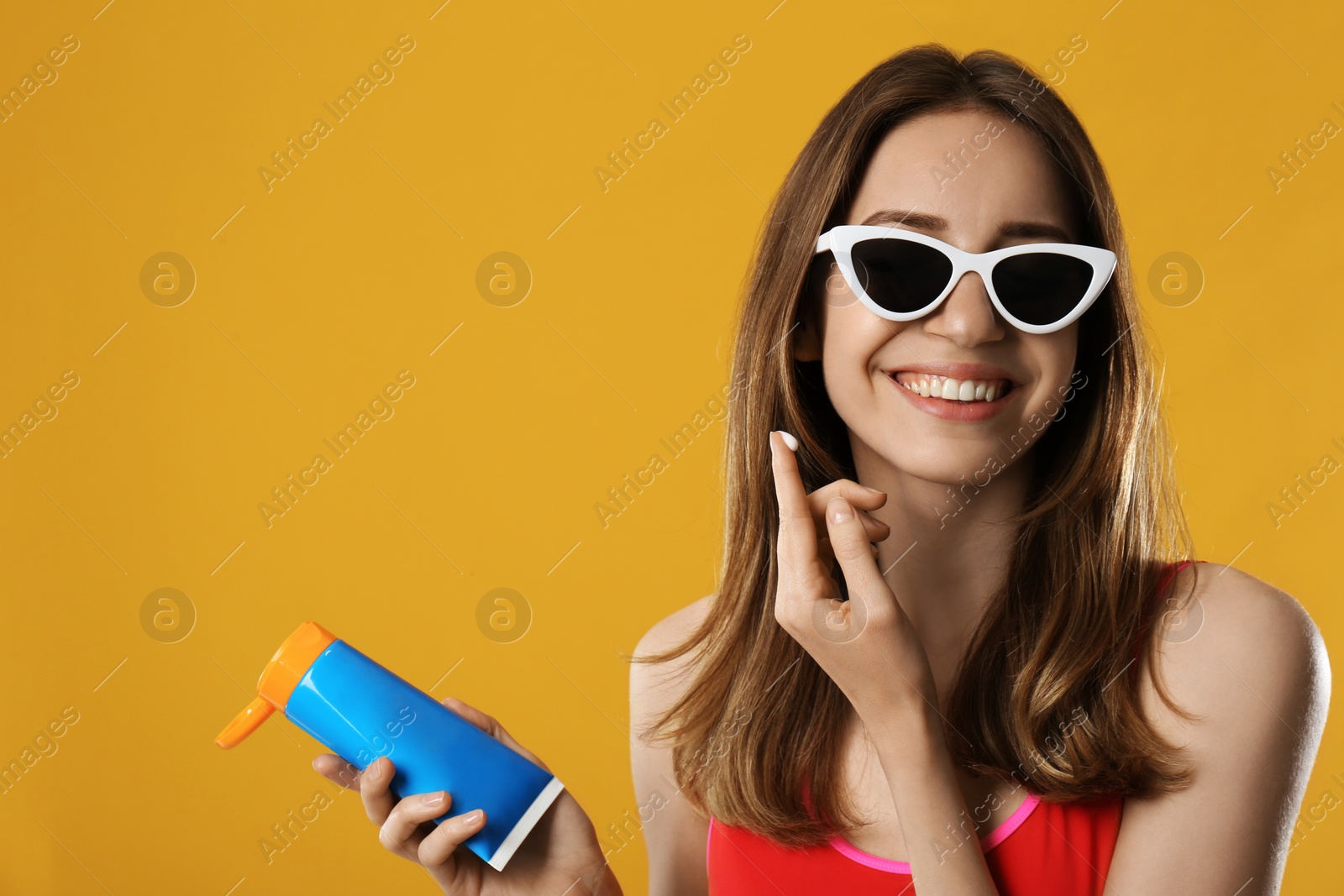 Photo of Young woman applying sun protection cream on orange background. Space for text