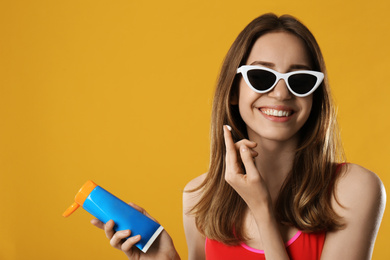 Young woman applying sun protection cream on orange background. Space for text