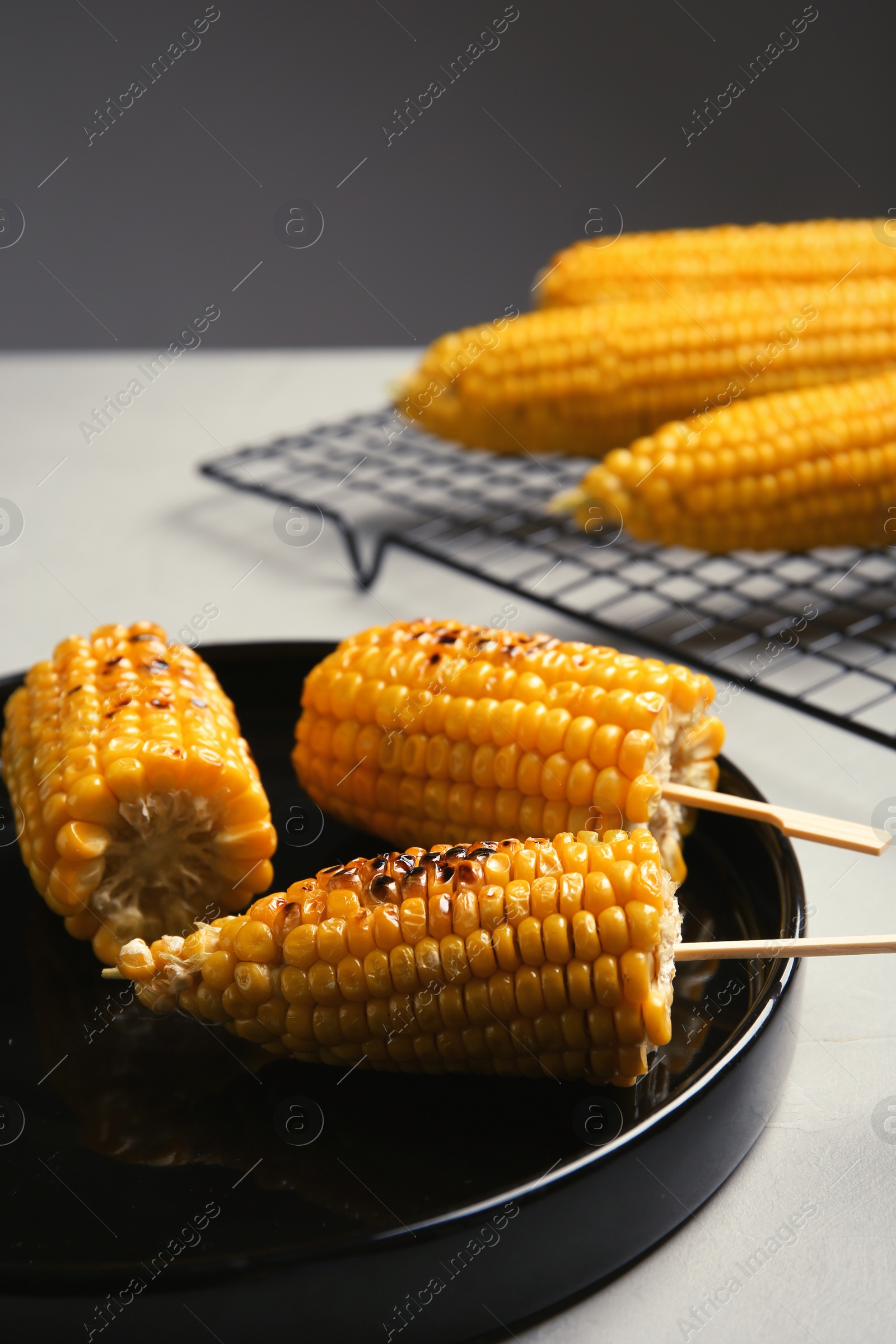 Photo of Ceramic plate with grilled corn cobs on light table