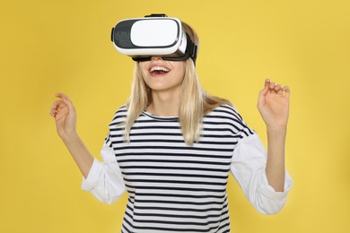 Photo of Emotional woman playing video games with virtual reality headset on color background