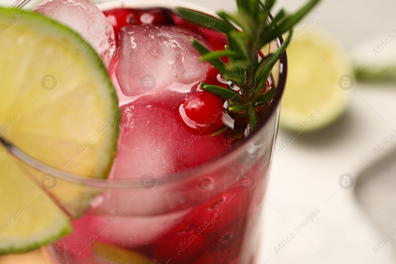 Photo of Tasty cranberry cocktail with rosemary and lime in glass on table, closeup