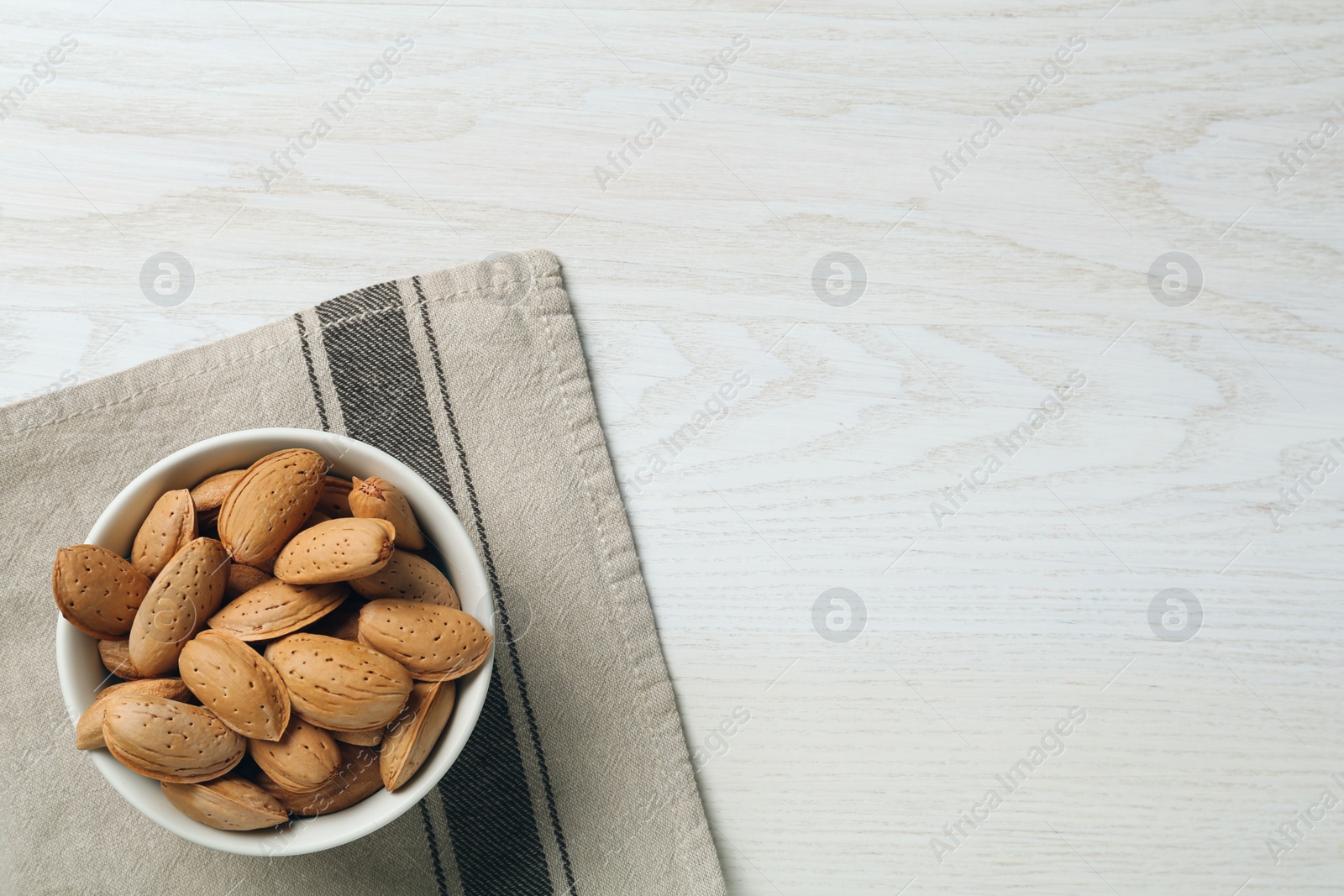 Photo of Ceramic bowl with almonds on white wooden table, top view and space for text. Cooking utensil