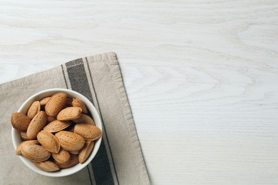 Photo of Ceramic bowl with almonds on white wooden table, top view and space for text. Cooking utensil