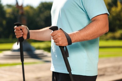 Photo of Man practicing Nordic walking with poles outdoors on sunny day, closeup