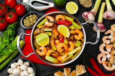 Photo of Saucepan with delicious Tom Yum soup and ingredients on black marble table, flat lay