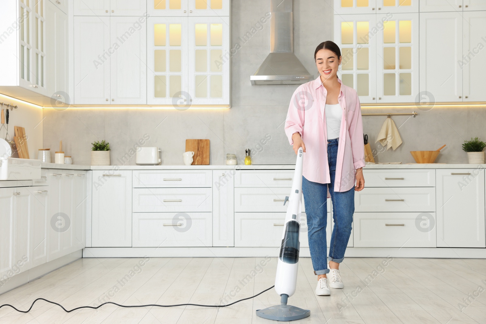 Photo of Happy woman cleaning floor with steam mop in kitchen at home. Space for text