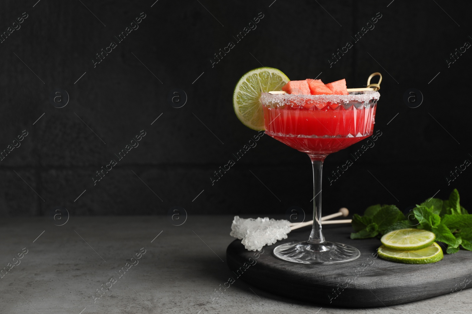 Photo of Cocktail glass of delicious fresh watermelon juice, lime and mint on grey table. Space for text