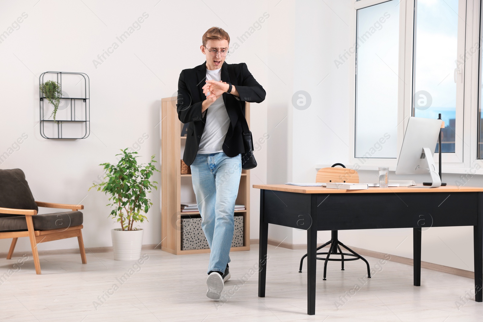 Photo of Emotional young man checking time while walking in office. Being late