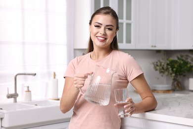 Photo of Happy woman with jug and glass of water in kitchen