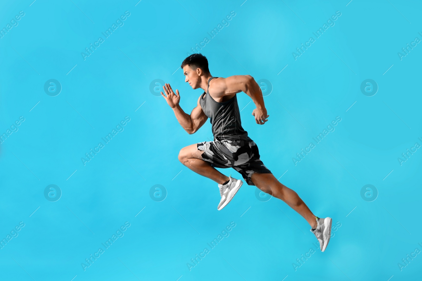 Photo of Athletic young man running on light blue background, side view