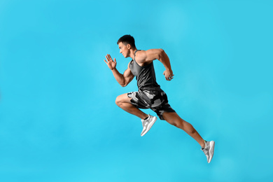 Photo of Athletic young man running on light blue background, side view