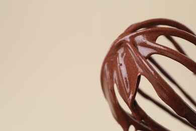 Whisk with chocolate cream on beige background, closeup. Space for text