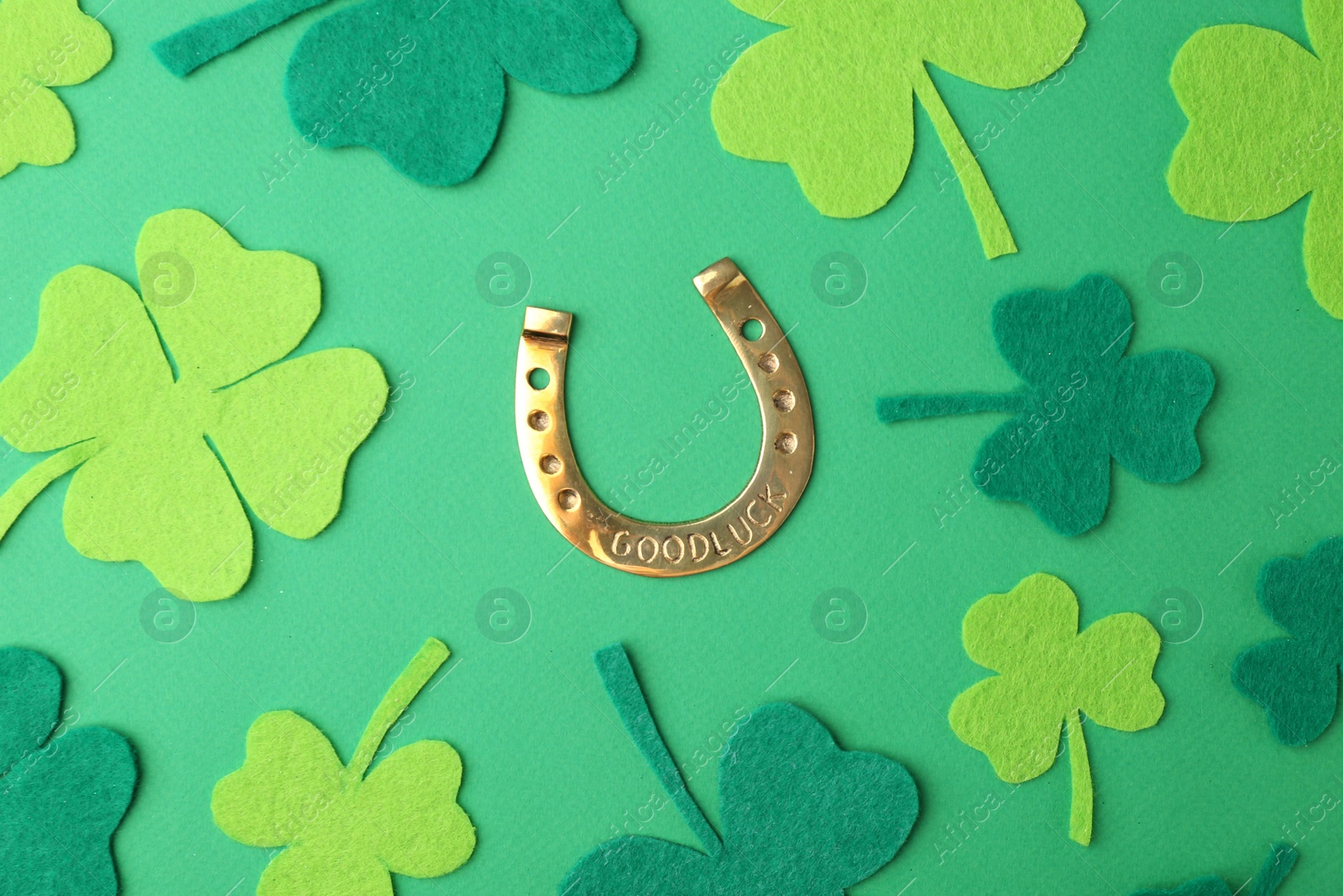 Photo of St. Patrick's day. Golden horseshoe and decorative clover leaves on green background, flat lay