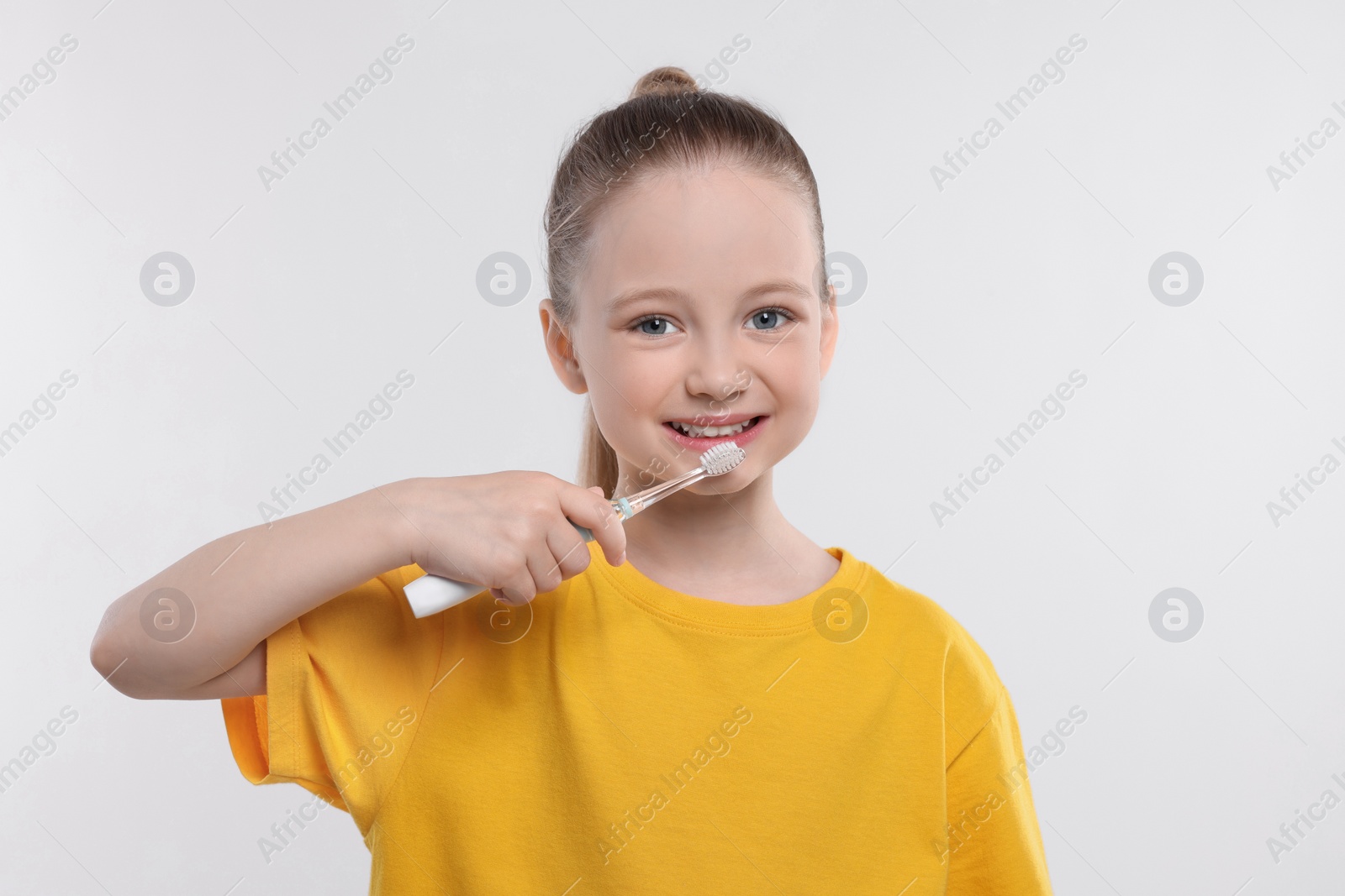 Photo of Happy girl brushing her teeth with electric toothbrush on white background