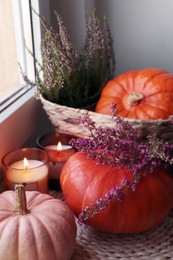 Photo of Wicker basket with beautiful heather flowers, pumpkins and burning candles near window indoors