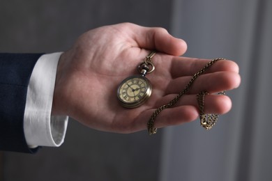 Photo of Man holding chain with elegant pocket watch on blurred background, closeup