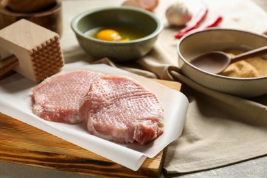 Photo of Raw pork chops, meat mallet and ingredients for cooking schnitzel on grey table, closeup