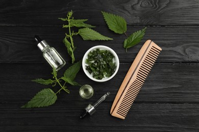 Photo of Stinging nettle, extract and comb on black wooden background, flat lay. Natural hair care