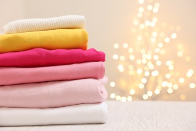 Photo of Stack of folded clothes on wooden table against beige background with blurred lights, space for text