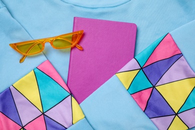 Photo of Stylish notebook and eyeglasses on color shirt, flat lay