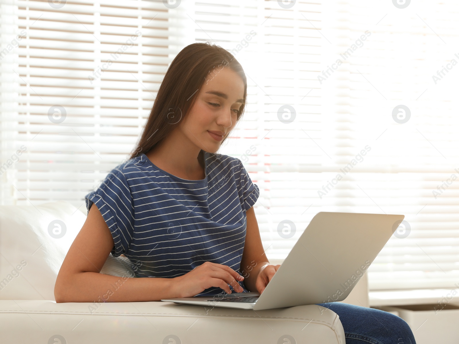 Photo of Young woman using laptop for search on sofa at home