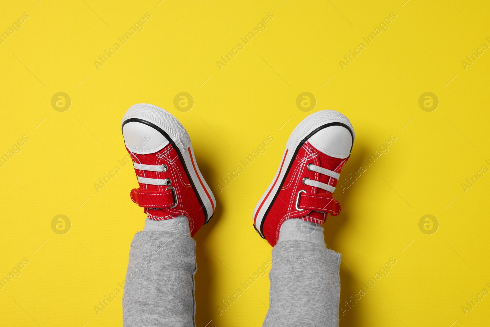 Photo of Little child in stylish red gumshoes on yellow background, top view