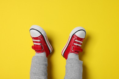 Little child in stylish red gumshoes on yellow background, top view