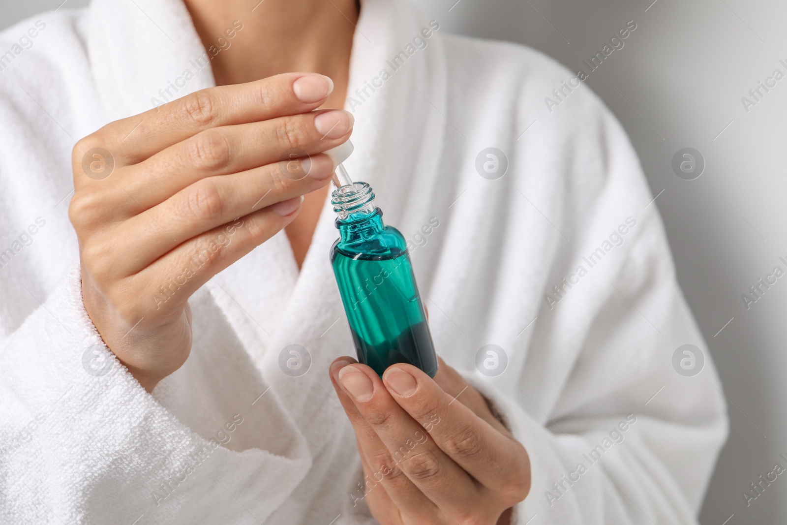 Photo of Woman with bottle of cosmetic serum and pipette on grey background, closeup