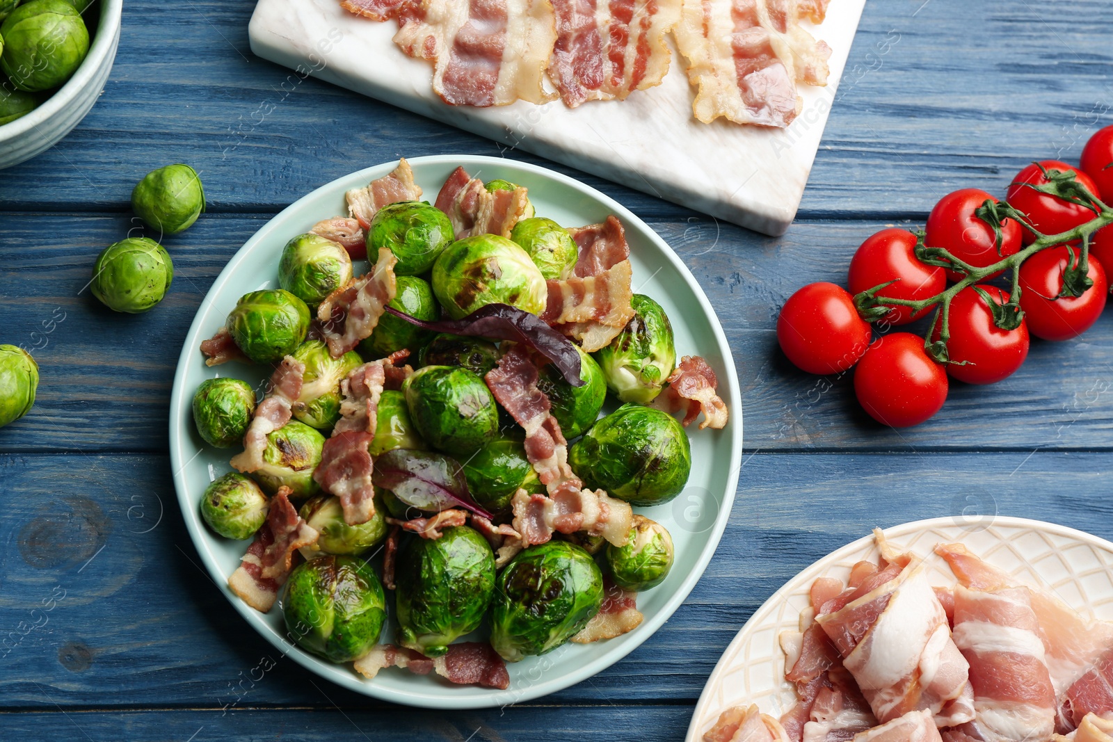 Photo of Delicious Brussels sprouts with bacon on blue wooden table, flat lay