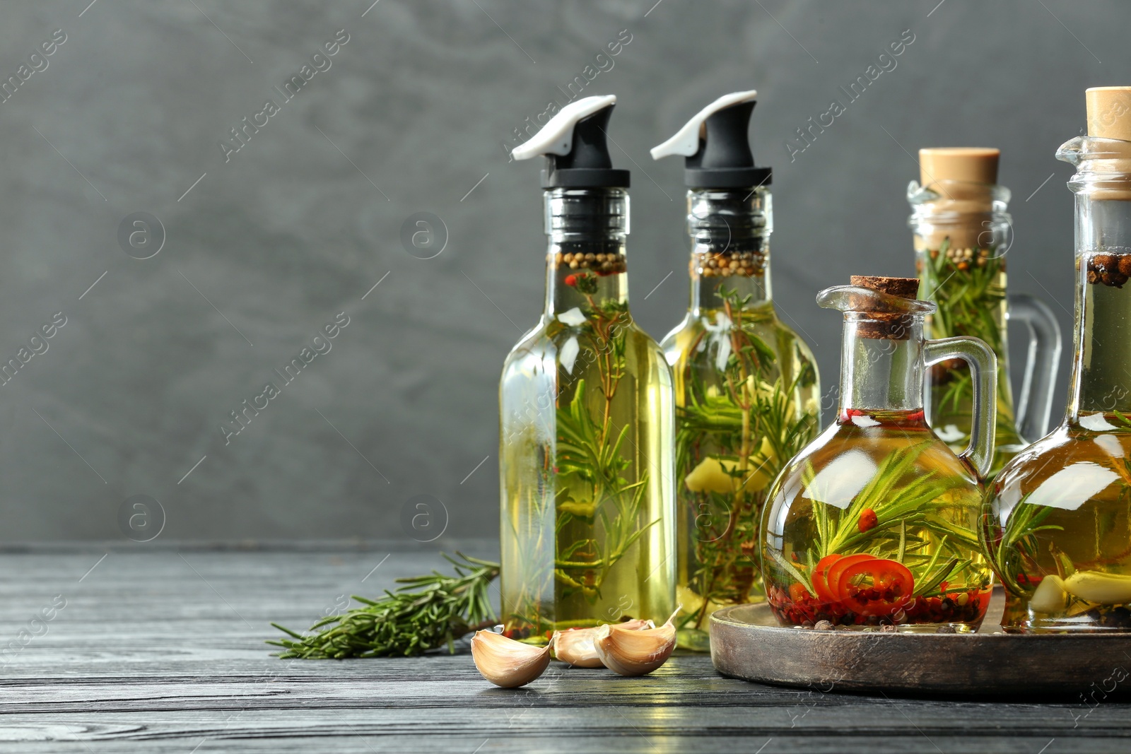 Photo of Cooking oil with different spices and herbs in bottles on grey wooden table. Space for text