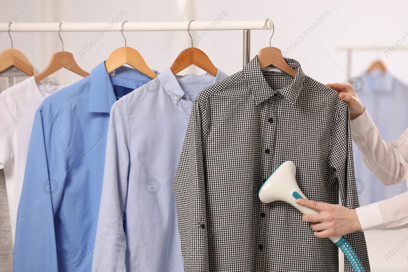 Photo of Woman steaming shirt on hanger in room, closeup