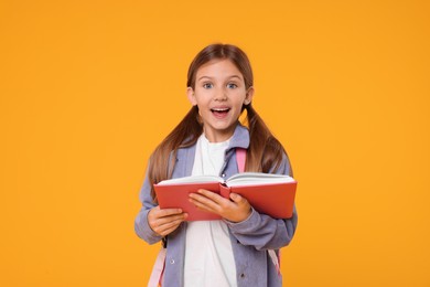 Photo of Happy schoolgirl with open book on orange background