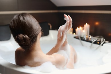 Photo of Young woman taking bubble bath, back view. Romantic atmosphere