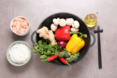 Photo of Wok, chopsticks and different products on grey textured table, flat lay