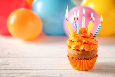 Photo of Delicious birthday cupcake with candles and blurred balloons on background