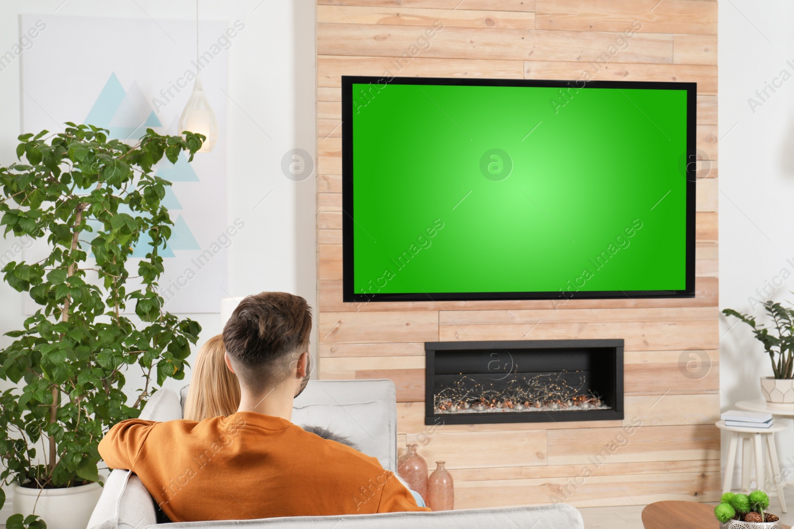 Photo of Couple watching TV on sofa in living room with decorative fireplace