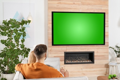 Photo of Couple watching TV on sofa in living room with decorative fireplace