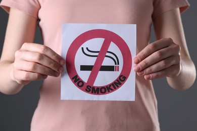 Photo of Woman holding card with no smoking sign on gray background, closeup