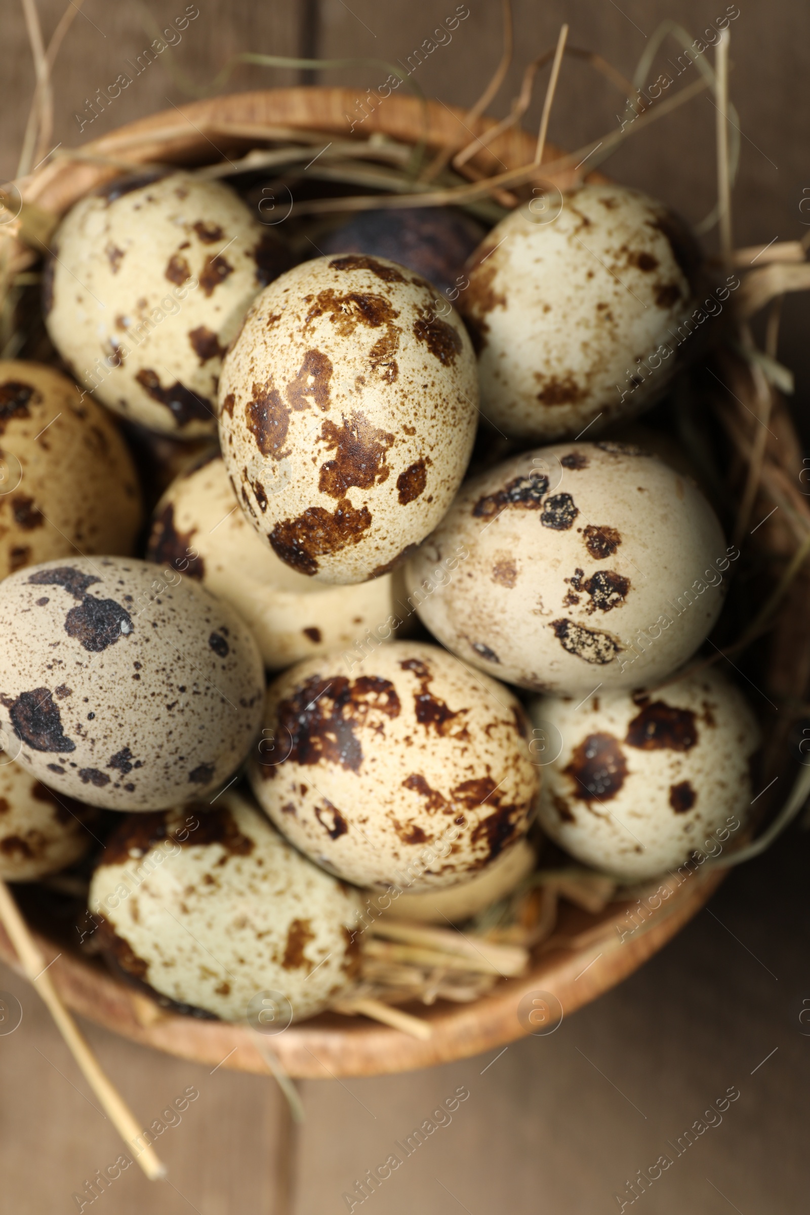 Photo of Wooden bowl with quail eggs and straw on table, top view