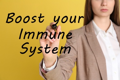 Image of Boost your immune system. Woman writing text on transparent board, closeup