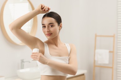 Beautiful young woman applying deodorant in bathroom