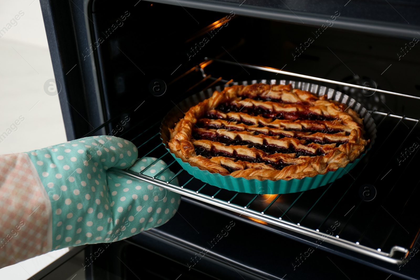 Photo of Person taking delicious fresh homemade cake out of oven indoors, closeup