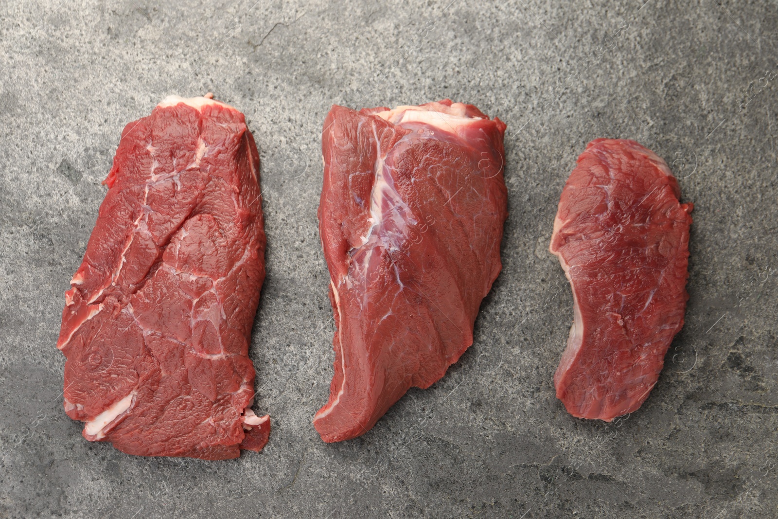 Photo of Pieces of raw beef meat on grey table, flat lay