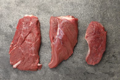 Photo of Pieces of raw beef meat on grey table, flat lay