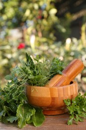 Photo of Mortar, pestle and different herbs on wooden table outdoors, space for text