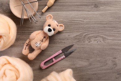 Felted bear, wool and different tools on wooden table, flat lay. Space for text