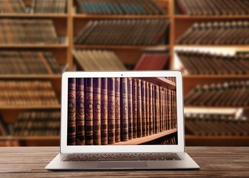 Image of Online library. Modern laptop on wooden table and shelves with books indoors