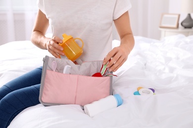 Woman packing baby accessories into maternity bag on bed, closeup